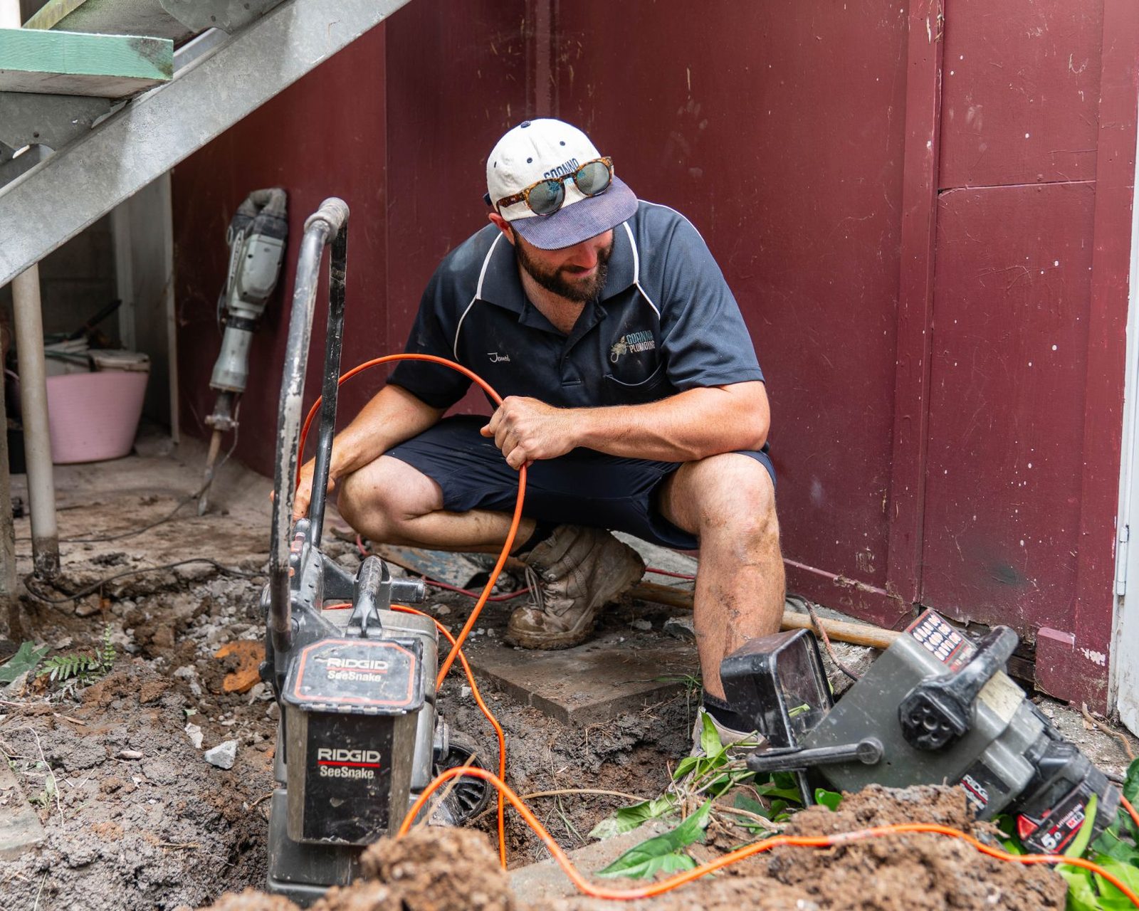 Jarred feeding a drain camera into a sewer line under a Queenslander